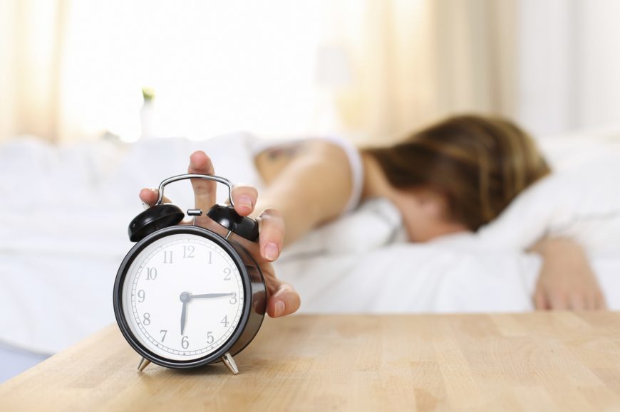 Sleepy young woman trying kill alarm clock