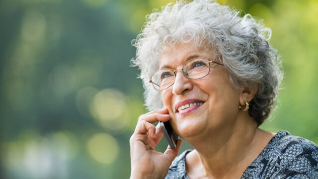 Portrait of mature woman talking on smartphone outdoor. Senior woman smiling and talking on the phone at park. Close up face of a cheerful elderly woman on phone call.